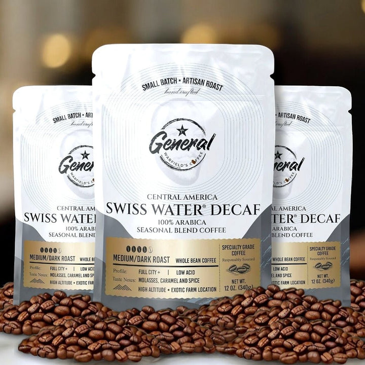 Three bags of General Warfield's Swiss Water Decaf Coffee sitting on fresh decaffeinated coffee beans.